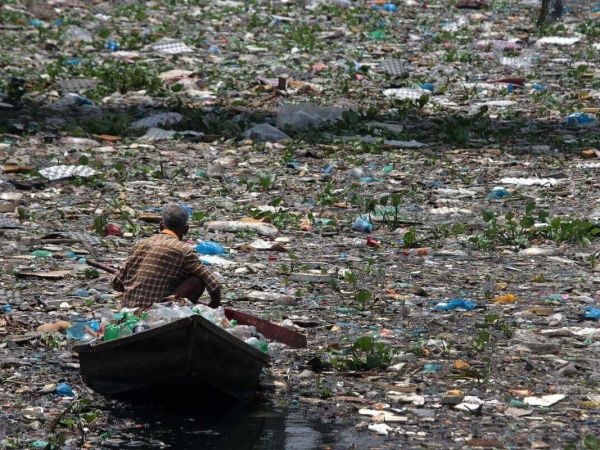 A Man rowing boat through river full of various waste